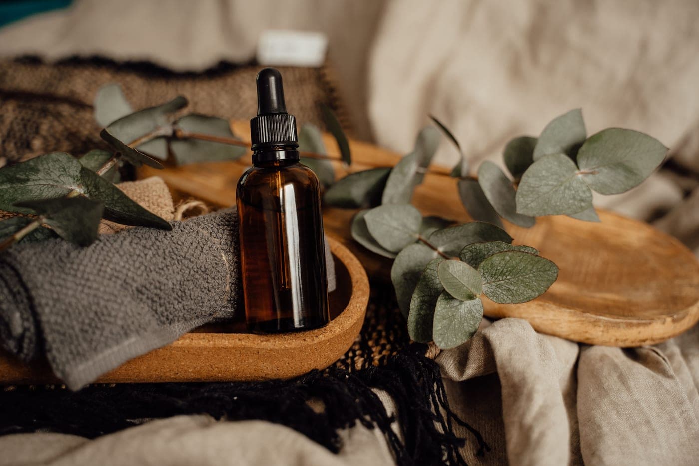 Amber glass massage oil bottle with eucalyptus on a wooden tray.