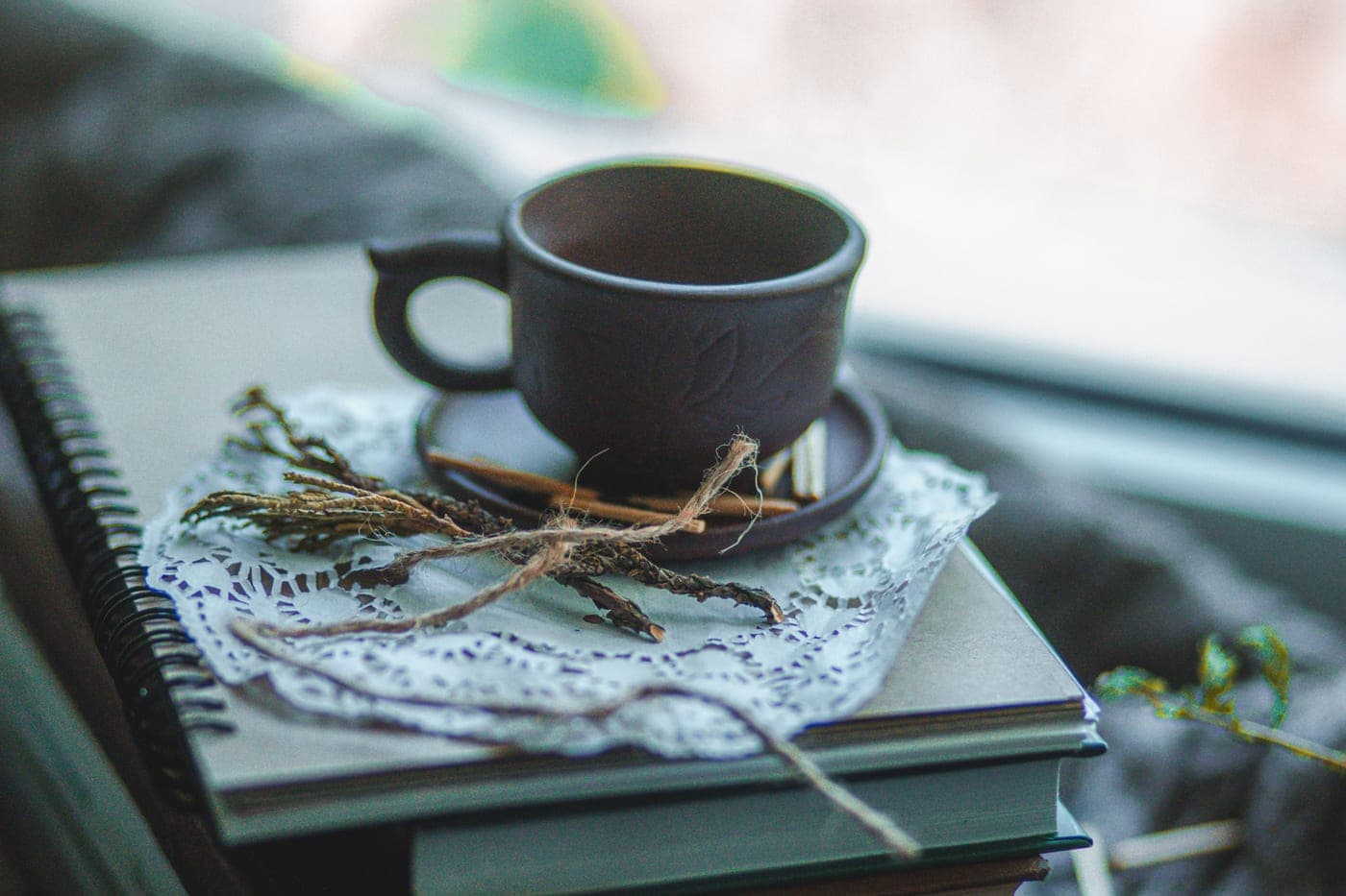 A ceramic cup resting on stacked notebooks in soft daylight.